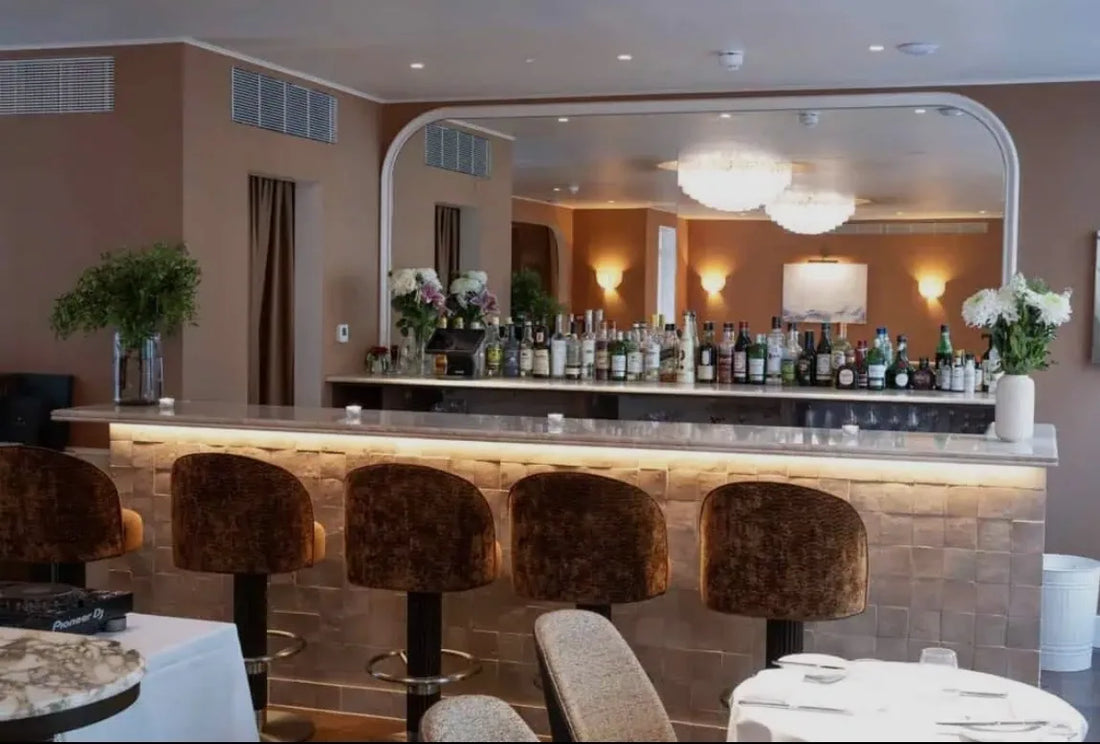 Restaurant bar with a counter front clad in terra original zellige tiles, velvet bar stools and an arched mirror